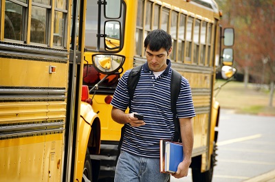 Teen Distracted by Cellphone Walking Near School Busses